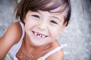 A child smiling showing her visible baby tooth in relation to pediatric tooth extractions.