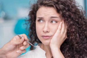 Young woman holding her cheek feeling pericoronitis symptoms and waiting to receive a pericoronitis treatment plan.