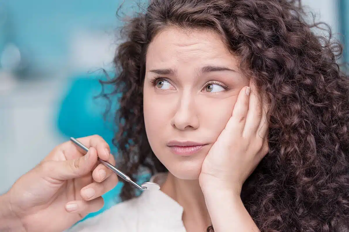 Young woman holding her cheek feeling pericoronitis symptoms and waiting to receive a pericoronitis treatment plan.