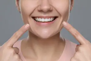 Close-up of a smiling person pointing to their corrected gummy smile after treatment.