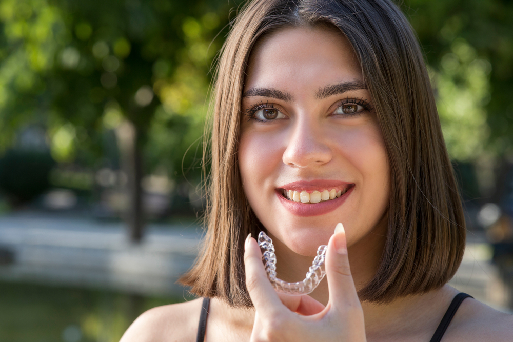 Smiling woman holding Invisalign aligner, exemplifying good oral hygiene practices.