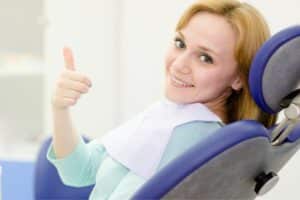 Smiling patient in a dental chair giving a thumbs-up, representing a comfortable dental implant procedure experience with sedation options.