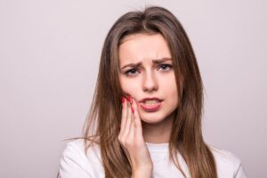 Woman touching her cheek in discomfort, highlighting gum disease symptoms and the need for periodontal treatment options.
