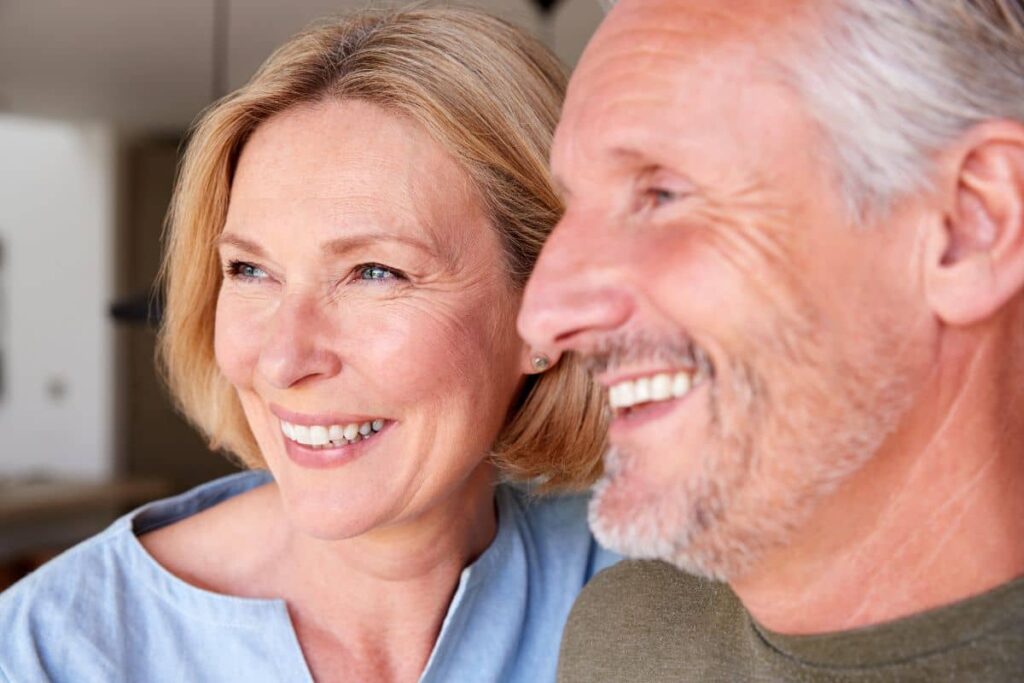 Happy older couple with healthy smiles indoors, symbolizing the long-term benefits and stability of dental implants.