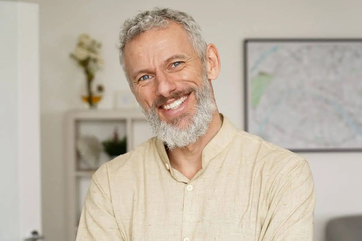 Older man with gray beard smiling confidently after dental implant treatment.
