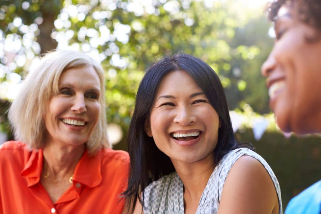 Group of women laughing outdoors, showing confident smiles supported by dental implants and improved oral health.