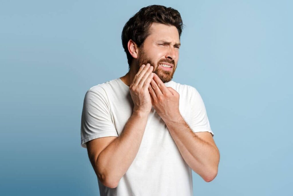 Man holding his jaw in discomfort, indicating possible complications after laser gum treatment like infection or pain.