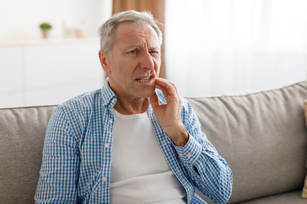 Older man touching his cheek, indicating gum discomfort, related to LANAP treatment for gum disease without surgery.