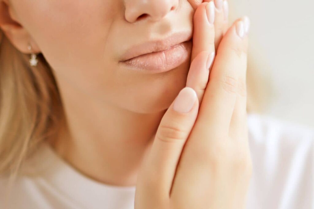 Woman pressing a swollen cheek, a possible sign of apical periodontitis or a dental abscess.